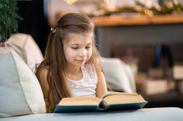 A little girl is reading an interesting book. Education and leisure of children. - Foto, imagen