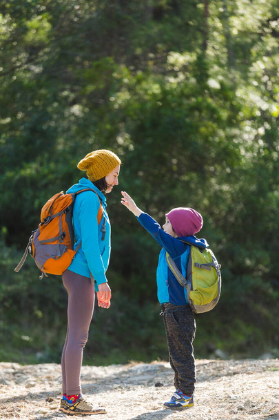 Chłopiec z plecakiem spaceruje po lesie z mamą, dziecko przytula mamę, kobieta podróżuje z dzieckiem, wsparcie matki, Dzień Matki. - Zdjęcie, obraz
