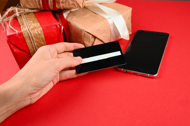 Hand holds a plastic card on the background of gifts. High quality photo - Photo, Image