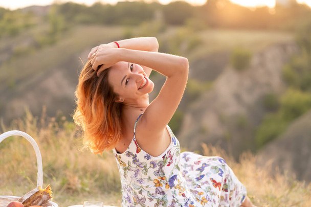 Něžná krásná rusovlasá dívka si užívá západ slunce na poli s kopcem - Fotografie, Obrázek