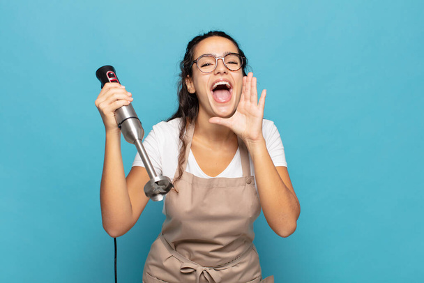 young hispanic woman feeling happy, excited and positive, giving a big shout out with hands next to mouth, calling out - 写真・画像