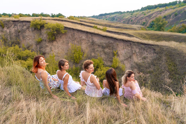A cheerful company of beautiful girls friends enjoy a picturesque panorama of the green hills at sunset. - Zdjęcie, obraz