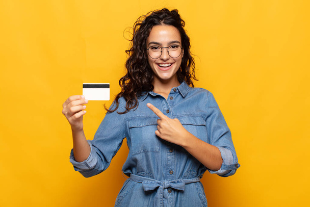 young hispanic woman smiling cheerfully, feeling happy and pointing to the side and upwards, showing object in copy space - Foto, Imagen