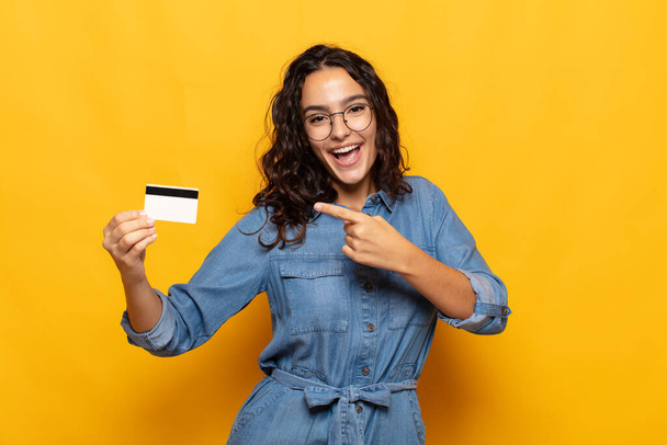 young hispanic woman looking excited and surprised pointing to the side and upwards to copy space - Photo, Image