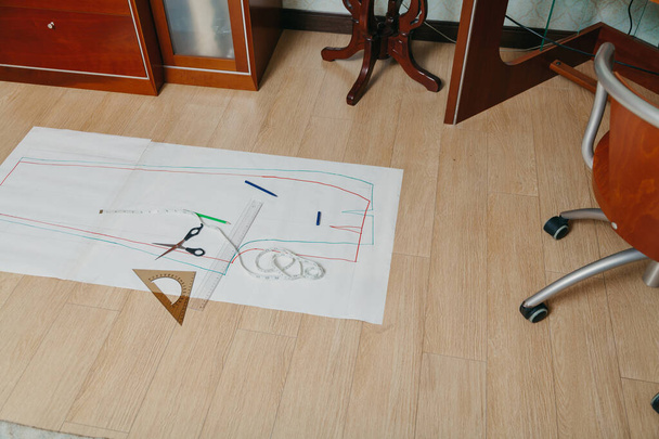 Sewing pattern lies on the floor. A silhouette of a garment is drawn on a paper sheet. On top is a ruler, scissors and a flexible centimete - Photo, image