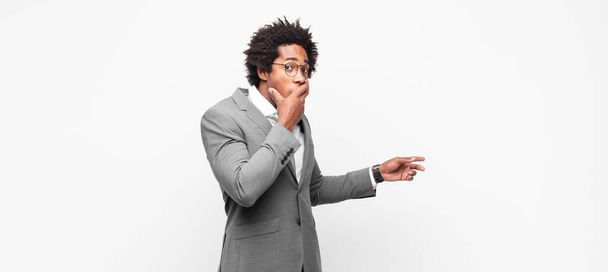 black afro businessmanfeeling happy, shocked and surprised, covering mouth with hand and pointing to lateral copy space - Фото, изображение