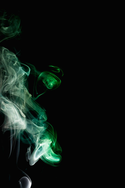 Whimsical curls and shapes of green smoke on a dark background. Streaming smoke from a burning incense stick. - Foto, imagen