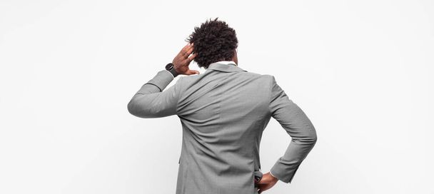 black afro businessmanfeeling clueless and confused, thinking a solution, with hand on hip and other on head, rear view - Fotoğraf, Görsel