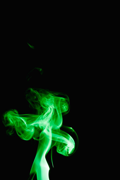 Caprichosos rizos y formas de humo verde sobre un fondo oscuro. Esparciendo humo de una varilla de incienso en llamas. - Foto, imagen