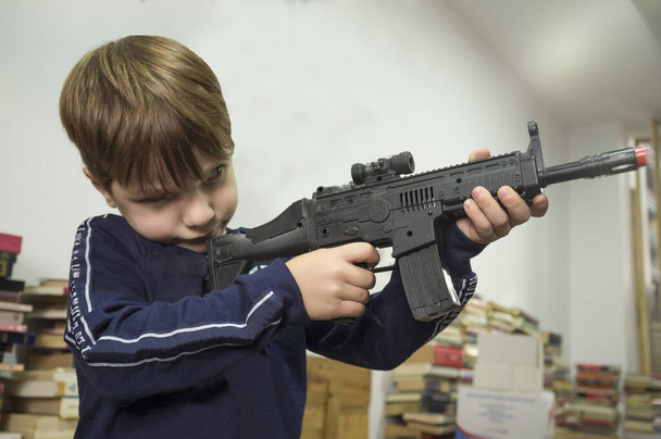 Vijf jaar kleine jongen spelen met aanvalsgeweer. Speelgoedpistolen concept. Selectieve focus - Foto, afbeelding