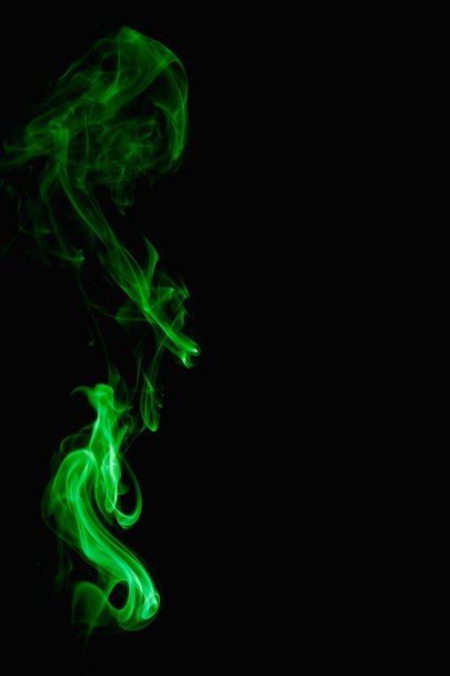 Whimsical curls and shapes of green smoke on a dark background. Streaming smoke from a burning incense stick. - Foto, afbeelding