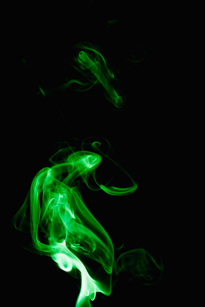 Grillige krullen en vormen van groene rook op een donkere achtergrond. Stroomt rook van een brandende wierookstaaf. - Foto, afbeelding