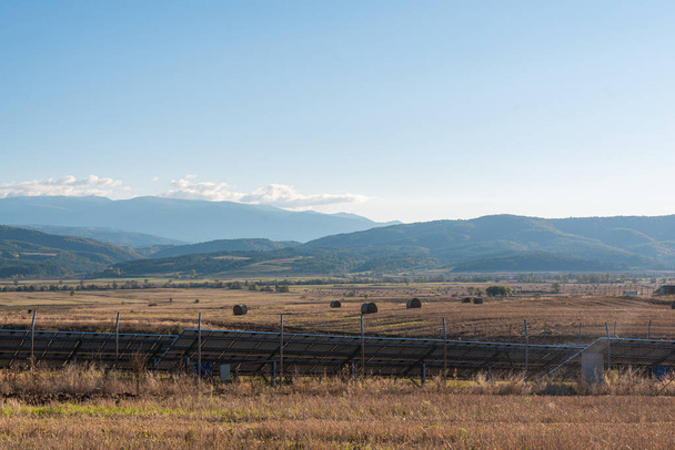 太陽光パネルステーションの横にある黄色の農地の収穫を見る人テキストブルガリア山の技術の棚田に散在する干し草の湾のコピースペース - 写真・画像