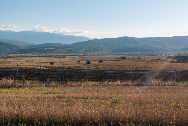 太陽光パネルステーションの横にある黄色の農地の収穫を見る人テキストブルガリア山の技術の棚田に散在する干し草の湾のコピースペース - 写真・画像