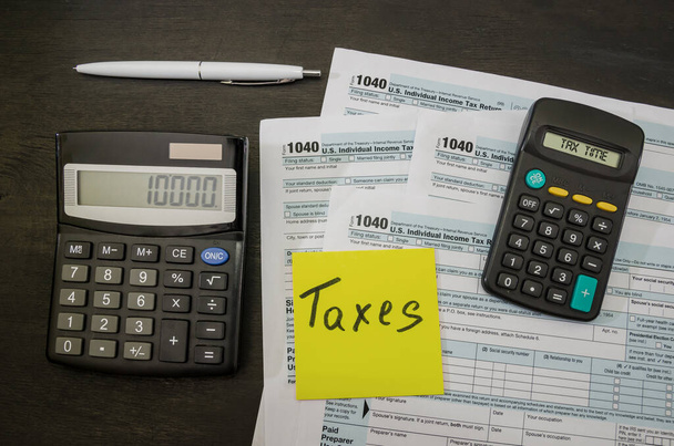 Steuerformulare 1040 mit Dollar, Aufkleber, Stift und Taschenrechner auf einem schwarzen Holztisch. Steuerzeitkonzept. Finanzdokument. - Foto, Bild