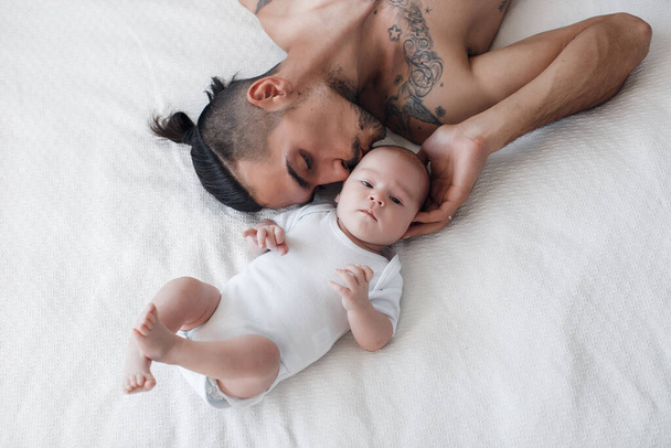 man with infant. happy family at home. happy father with cute two months baby boy laying in light bed at home - Foto, immagini