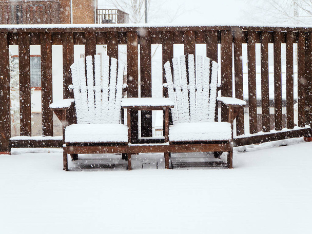 Two wooden garden chairs sit on a terrace covered with snow in winter during snowfall - Photo, Image