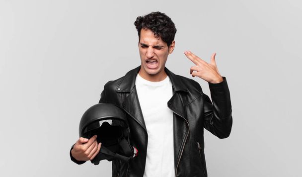 young handsome man looking unhappy and stressed, suicide gesture making gun sign with hand, pointing to head. motorbike rider concept - Фото, изображение