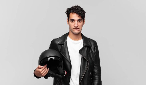 young handsome man looking puzzled and confused, biting lip with a nervous gesture, not knowing the answer to the problem. motorbike rider concept - Foto, immagini