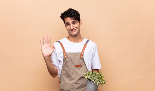 young gardener man smiling happily and cheerfully, waving hand, welcoming and greeting you, or saying goodbye - Foto, immagini