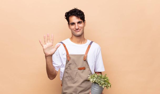young gardener man smiling and looking friendly, showing number five or fifth with hand forward, counting down - Foto, immagini
