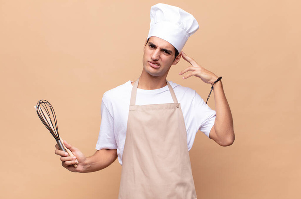 young baker man feeling confused and puzzled, showing you are insane, crazy or out of your mind - Фото, изображение