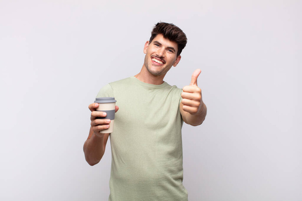 молодий чоловік з кавою відчуває себе гордим, безтурботним, впевненим і щасливим, позитивно посміхаючись з великими пальцями вгору
 - Фото, зображення