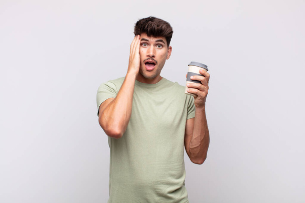 young man with a coffee feeling happy, excited and surprised, looking to the side with both hands on face - Fotoğraf, Görsel