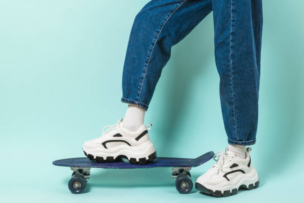 Un bambino in scarpe da ginnastica con la suola alta e lo skateboard su sfondo blu. Stile sportivo. Posto per testo. - Foto, immagini
