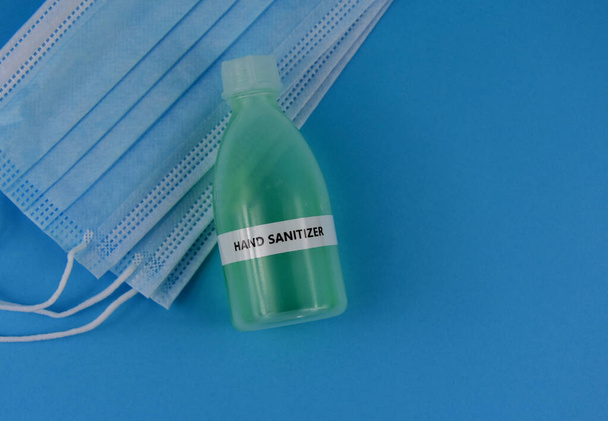 Hand sanitizer gel with protective face mask top view stock images. Protective equipment against COVID-19. Sanitizer gel bottle with medical mask isolated on a blue background with copy space for text - Photo, Image