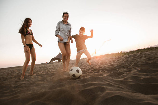 Glückliche Familie spielt Fußball am Strand und genießt schöne Familienzeit in den Sommerferien. - Foto, Bild