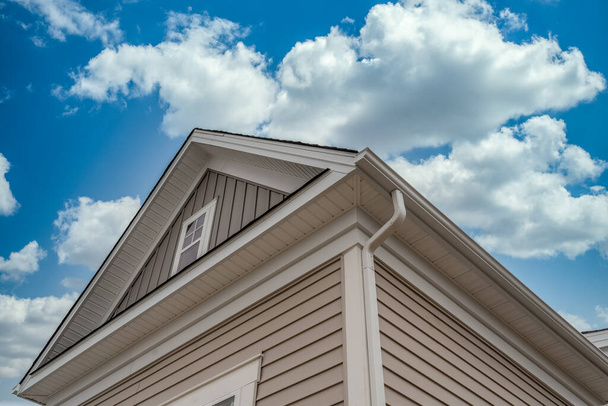 Système de garde de gouttière à ossature blanche, avec fascia gris horizontal et vertical en vinyle, bord goutte à goutte, soffit, sur un grenier à toit incliné dans un luxueux toit américain unifamilial ciel nuageux bleu - Photo, image