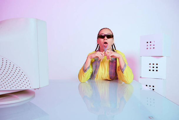 Stylish female office worker in sunglasses with obsolete computer and scissors shows tongue. Colored Neon light - Foto, Bild