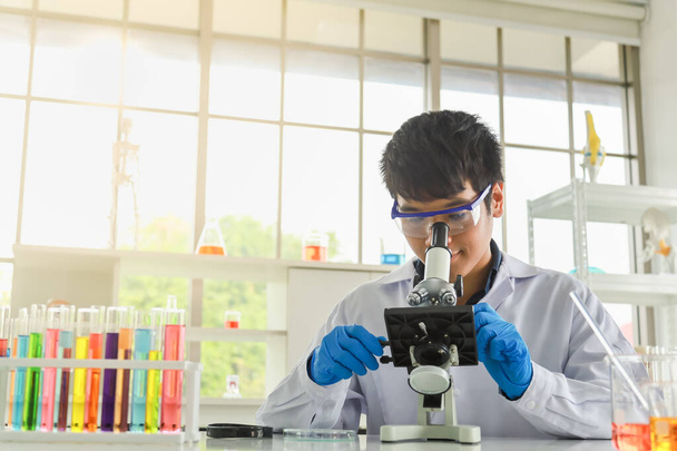 Jonge Aziatische professionele arts wetenschapper met een bril en blauwe rubberen handschoenen met behulp van microscoop en onderzoek in het werklaboratorium. Concept wetenschap en gezondheidszorg. - Foto, afbeelding