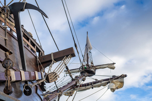 Anchor, masts and rigging of old pirate ship on background of cloudy blue sky. - Photo, Image