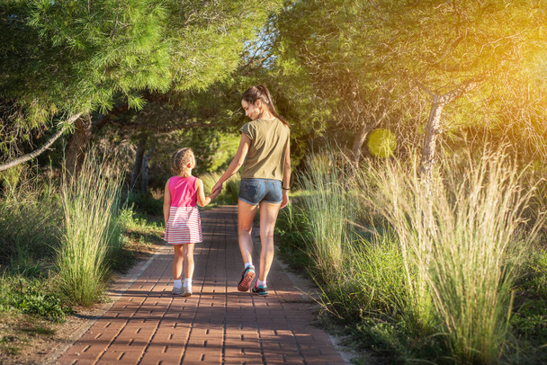 Όμορφη μητέρα και η κορούλα της έξω. Η όμορφη μαμά και το παιδί της περπατούν μαζί στο πάρκο το ηλιοβασίλεμα. Εξωτερική Πορτρέτο της ευτυχισμένης οικογένειας. Ημέρα της Μητέρας. - Φωτογραφία, εικόνα