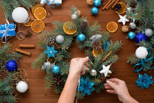 step-by-step process of making a Christmas tree wreath at home from spruce branches, oranges and Christmas balls in the silver and blue colors of the 2021 bull . wooden background top view. - Фото, зображення