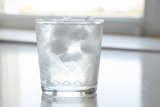vidrio transparente con hielo en el sol de la mañana en la mesa blanco - Foto, imagen