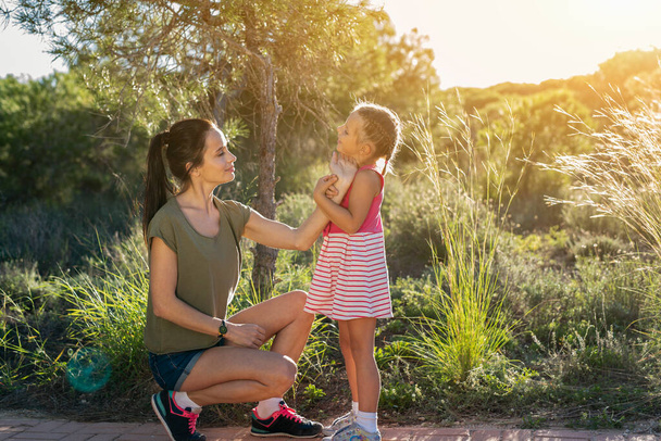 Beautiful mother and her little daughter outdoors. Beauty Mum and her Child sitting on Park pathway together at sunset. Outdoor Portrait of happy family. Mother's Day. - Foto, Imagen