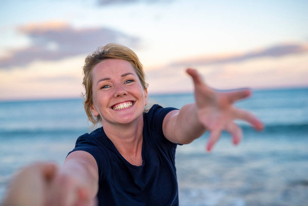 Seuraa minua onnellinen nuori nainen vetämällä kaveri käsi tavoittaa hänen ystävänsä auringonlaskun merenrannalla käsite huoleton modernin elämän. - Valokuva, kuva