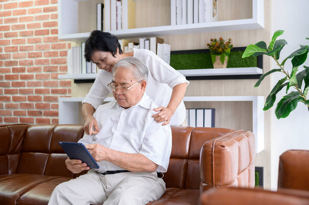 A happy senior Asian couple is using tablet and talking with family on webcam at home, retirement concept. - Foto, imagen
