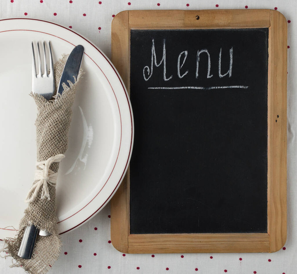 Menu title written white chalk on blackboard with table setting knife and fork lying on tablecloth polka dot. Copy space for your text.  - Φωτογραφία, εικόνα