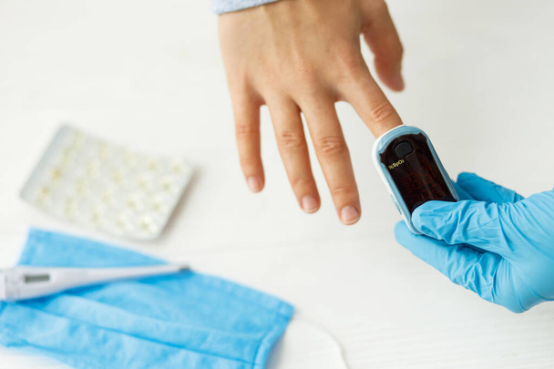 Врач измеряет уровень кислорода в крови с помощью переносного пульсоксиметра на женской руке в клинике или доме, тестирует насыщение кислородом, обнаруживает коронавирус, поврежденные легкие и пневмонию по вирусу - Фото, изображение