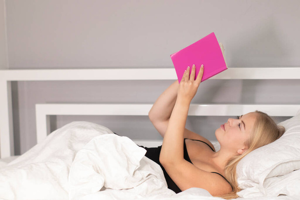 aantrekkelijk blond schrijven of lezen van een notitieboekje in witte slaapkamer. slim meisje - Foto, afbeelding