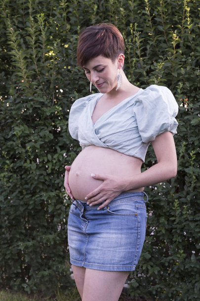 Fiatal terhes nő, zöld háttérrel. Anyaság. - Fotó, kép