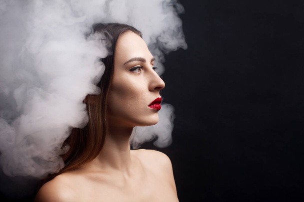 Attractive young girl and white smoke. Black background. - Фото, изображение