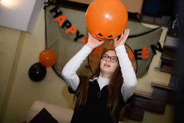 Chica en el sombrero de Halloween se está divirtiendo y jugando con balones de Halloween naranja y negro. Los niños se preparan para celebrar Halloween en casa, decorar el hogar - Foto, Imagen