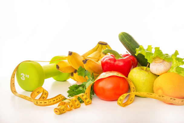 fresh fruits and vegetables on a white background, apples, tomatoes, lemon, garlic, cucumber, pepper, bananas, lettuce leaves , yellow measuring tape, green dumbbell - Valokuva, kuva
