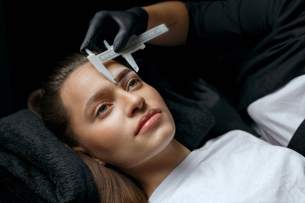 Brow stylist que mede sobrancelhas com a régua antes do procedimento microblading em um salão de beleza - Foto, Imagem