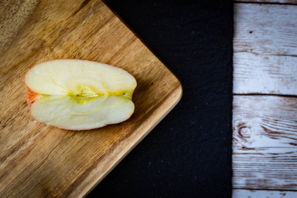 Jablečný plátek umístěný na dřevěné řezací desce nad černým kamenem na dřevěném stole - Fotografie, Obrázek